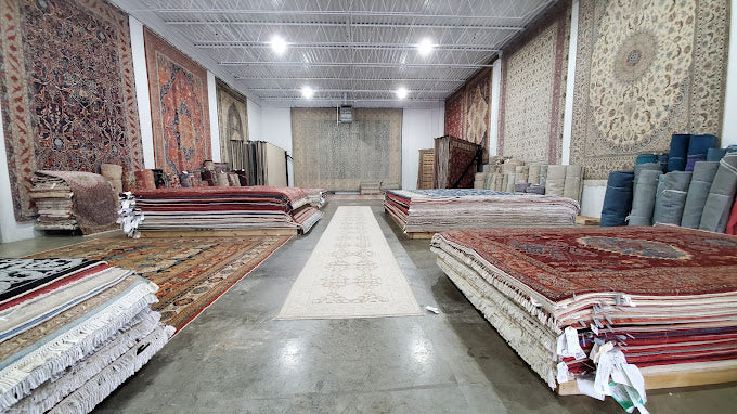 The Malik family rug showroom and distribution house in Chantilly, Virginia — hand-knotted rugs rolled and stacked across the floor with rugs displayed on the walls