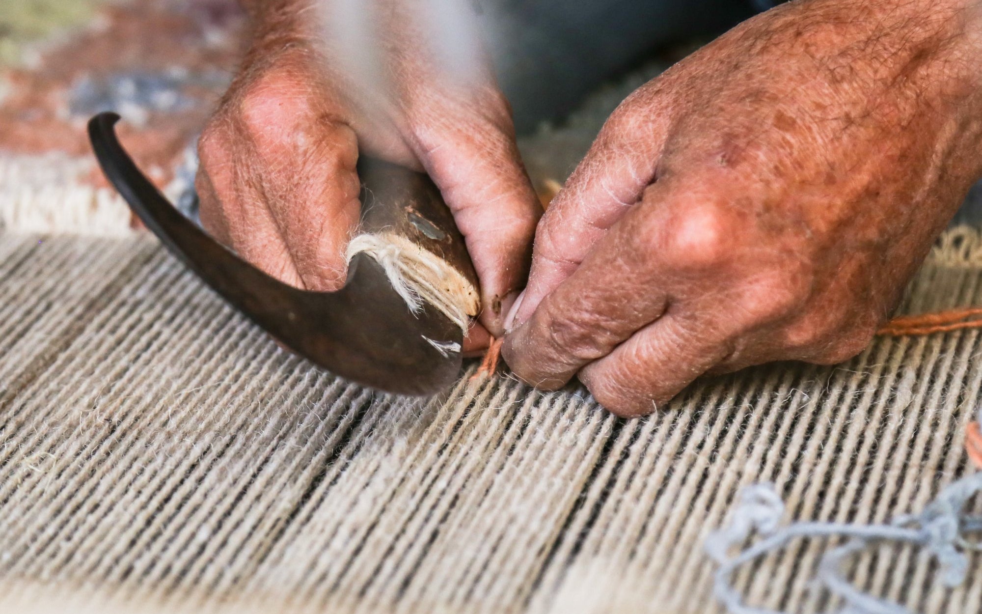 Hands tying knots on the loom with a traditional hook while weaving a hand-knotted rug