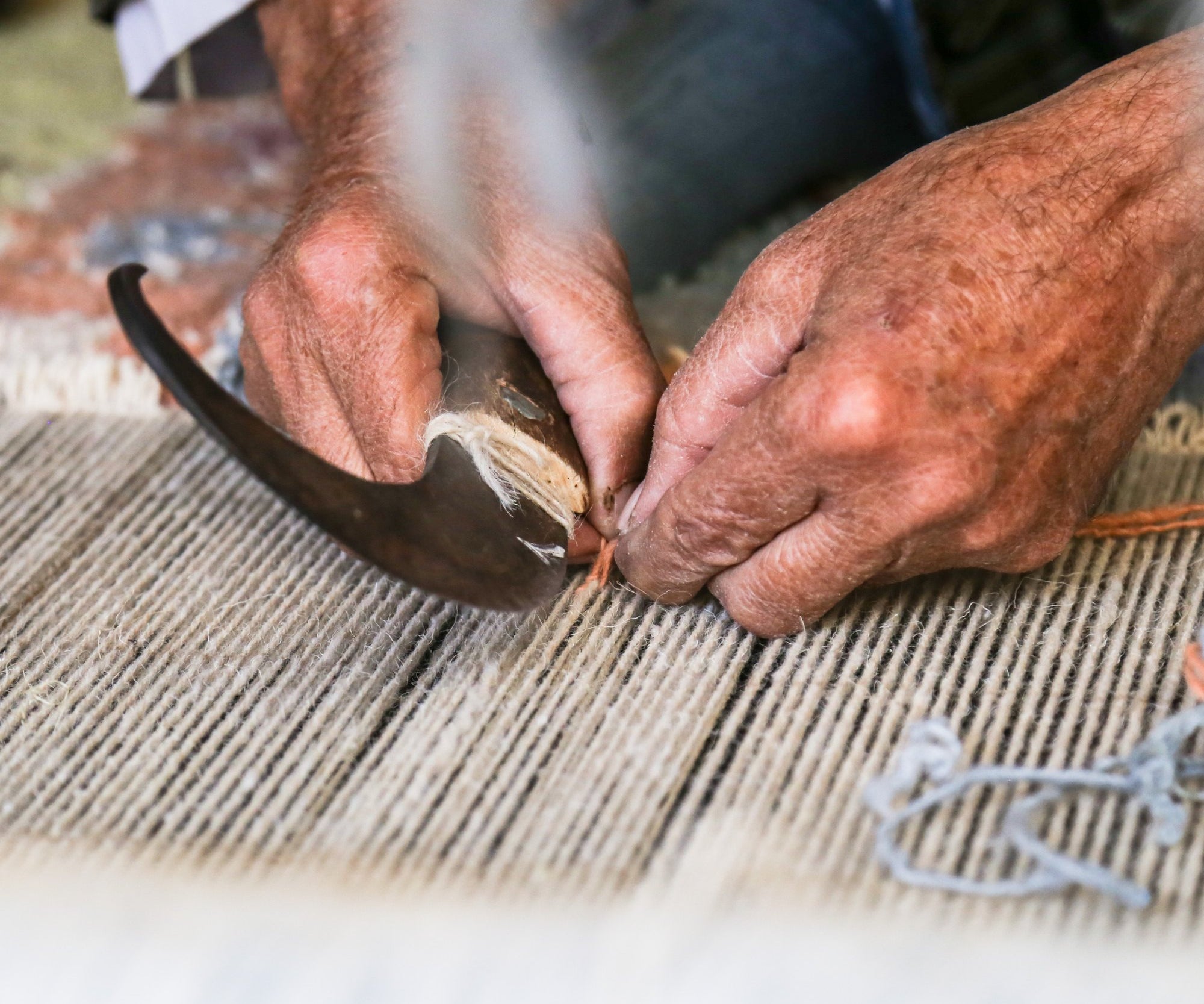 Hands tying knots on the loom with a traditional hook while weaving a hand-knotted rug