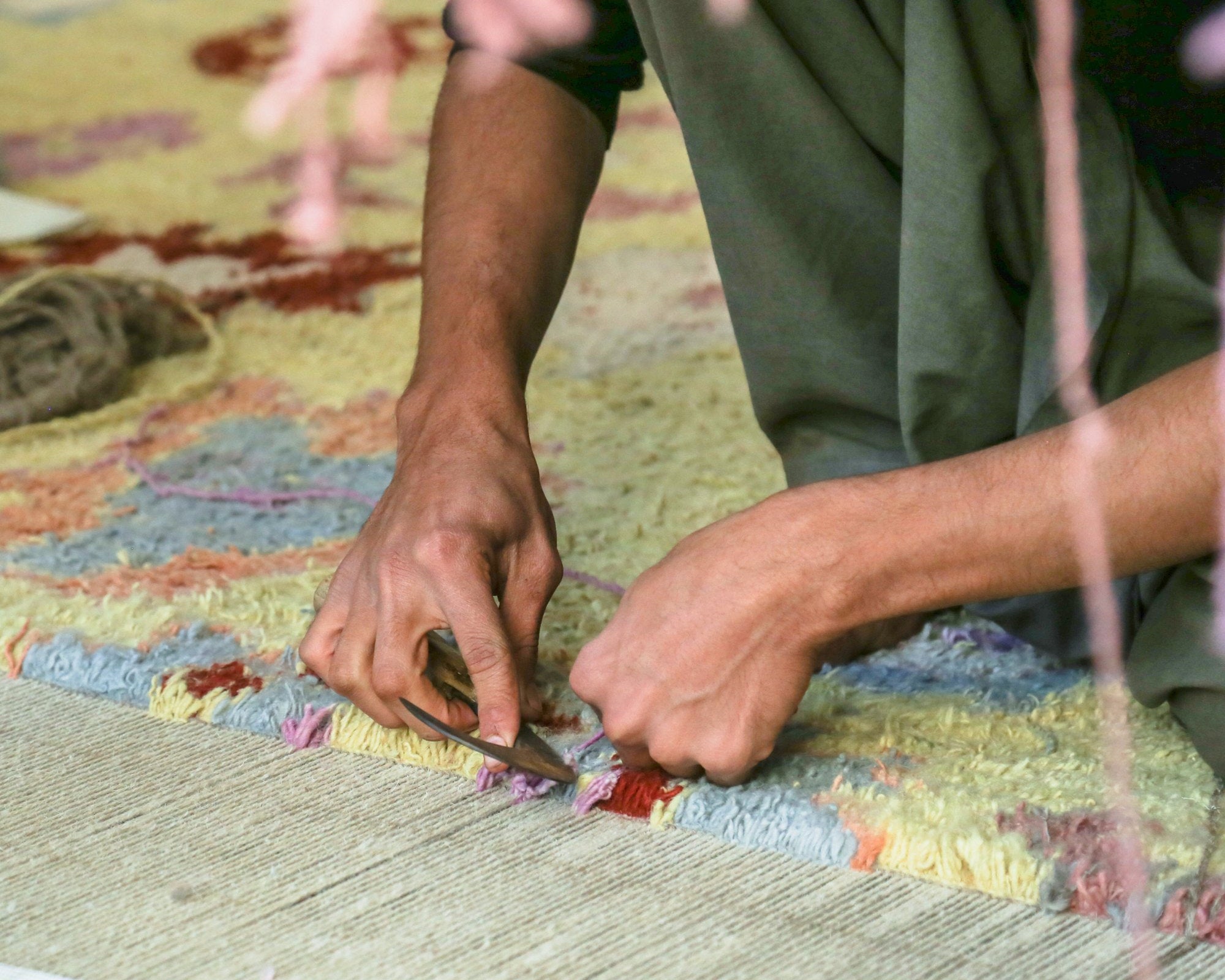 Hands shearing the pile of a hand-knotted rug on the loom with traditional shears