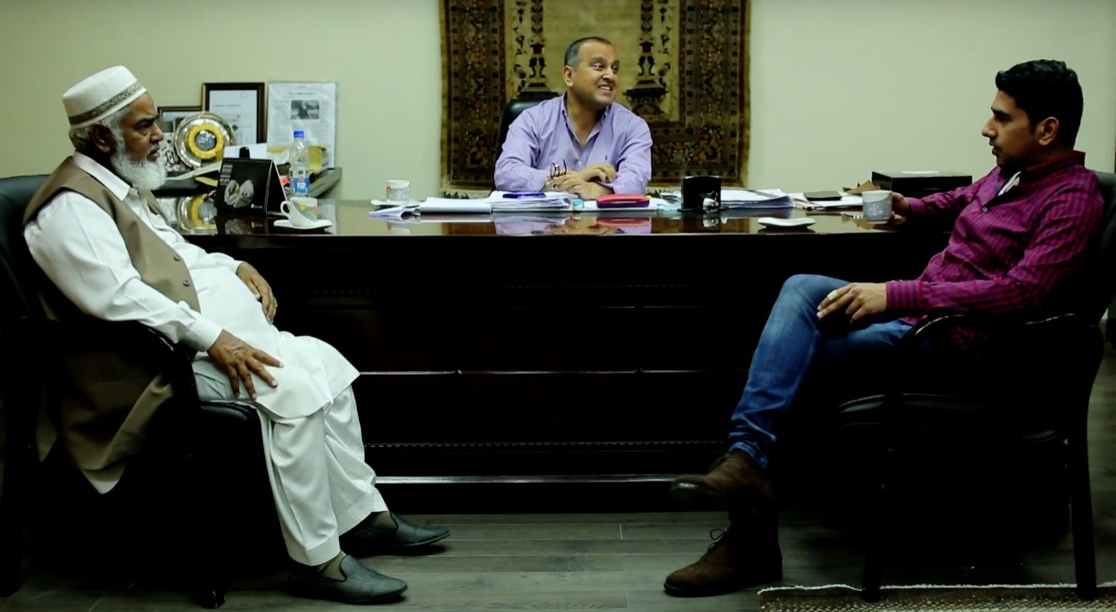 Three generations of the Malik family — Abdul Majeed Malik, his son Nadeem Malik, and grandson Hashim Malik — at the family rug business in Pakistan